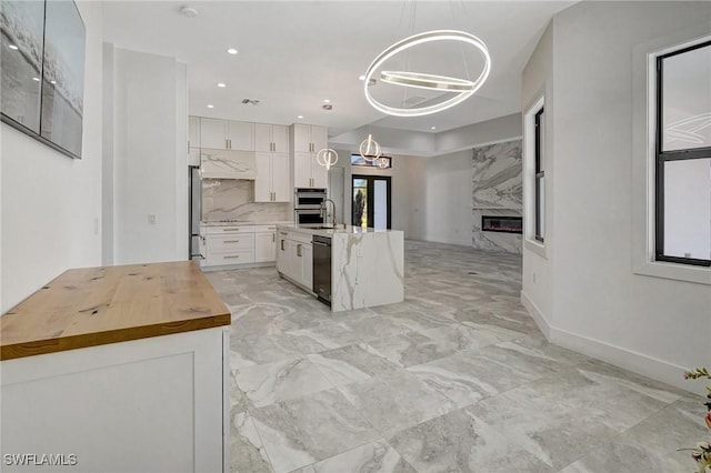 kitchen featuring under cabinet range hood, butcher block countertops, a premium fireplace, an inviting chandelier, and white cabinetry