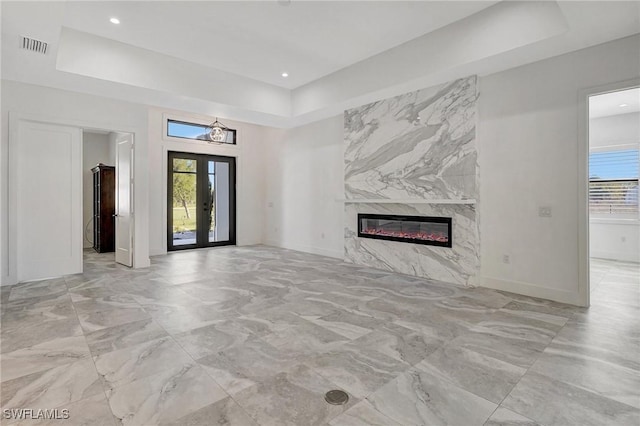 unfurnished living room with baseboards, a tray ceiling, a premium fireplace, recessed lighting, and french doors