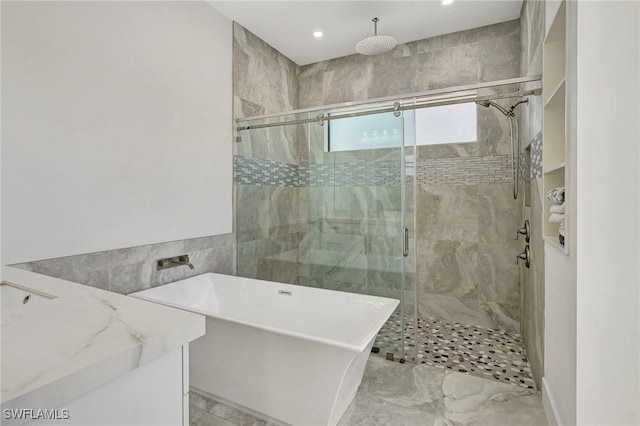 bathroom with tile walls, a stall shower, a freestanding bath, and vanity