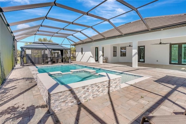 view of swimming pool featuring glass enclosure, a patio, a ceiling fan, a pool with connected hot tub, and french doors