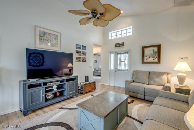 living room with light wood-type flooring, a towering ceiling, visible vents, and a ceiling fan