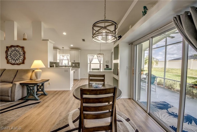 dining area with light wood-type flooring, an inviting chandelier, baseboards, and recessed lighting