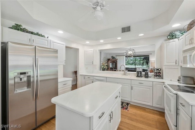 kitchen with visible vents, a sink, a tray ceiling, a center island, and white appliances