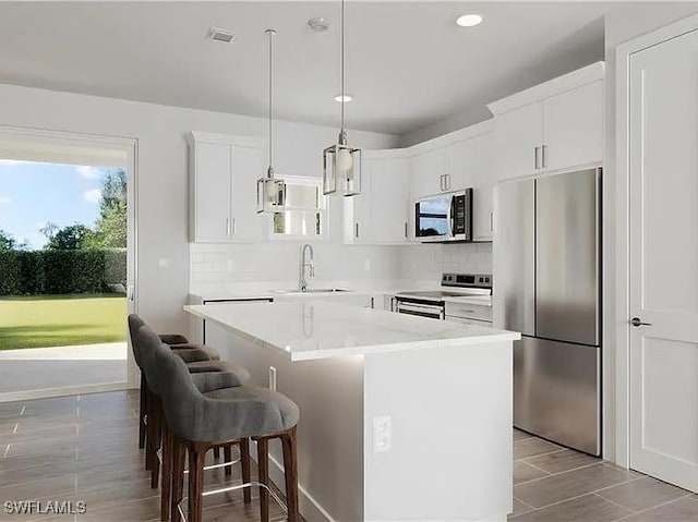 kitchen with a sink, appliances with stainless steel finishes, a kitchen bar, backsplash, and a center island