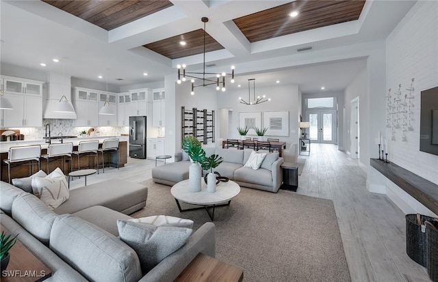 living room with light wood finished floors, visible vents, coffered ceiling, an inviting chandelier, and french doors