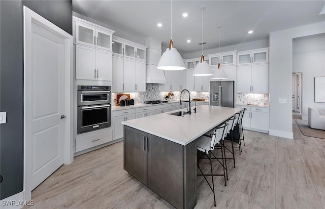 kitchen with light wood finished floors, custom exhaust hood, a spacious island, appliances with stainless steel finishes, and a sink