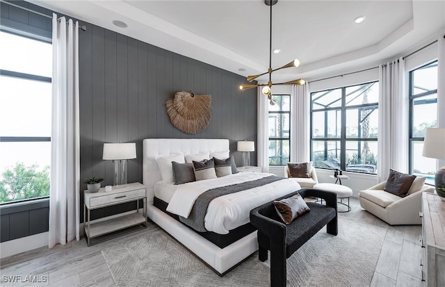 bedroom with recessed lighting, a raised ceiling, a notable chandelier, and light wood-style flooring