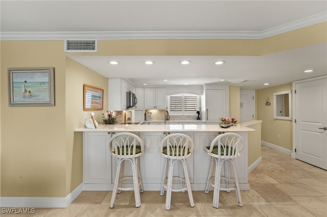 kitchen featuring visible vents, stainless steel microwave, a kitchen breakfast bar, a peninsula, and crown molding