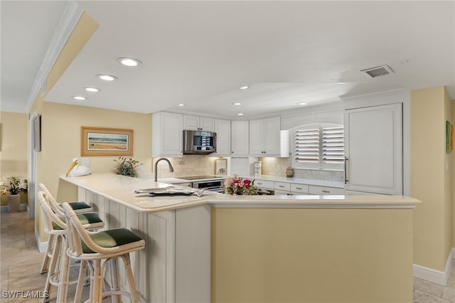 kitchen with crown molding, decorative backsplash, appliances with stainless steel finishes, a peninsula, and white cabinets