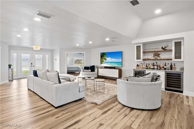 living area featuring a bar, light wood finished floors, visible vents, and french doors