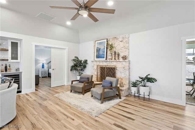 sitting room with beverage cooler, baseboards, light wood-style flooring, a bar, and a fireplace