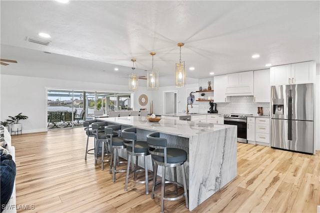 kitchen featuring light stone counters, stainless steel appliances, visible vents, white cabinetry, and backsplash