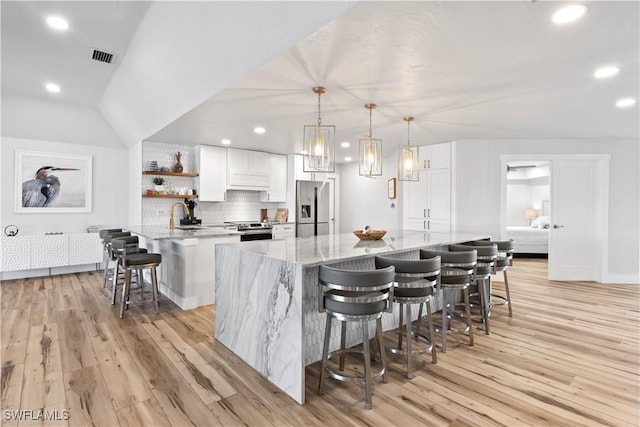 kitchen featuring white cabinets, light wood-style floors, a kitchen bar, and stainless steel appliances