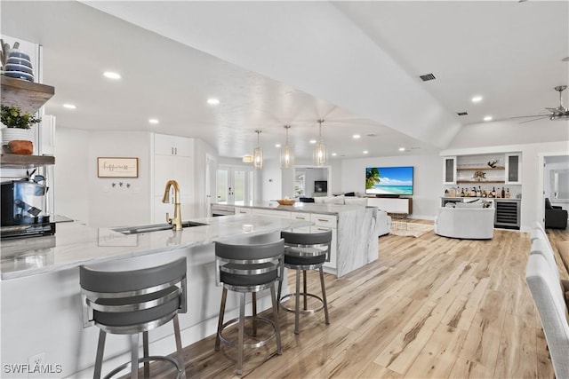 kitchen featuring light stone counters, visible vents, a sink, light wood-type flooring, and a peninsula