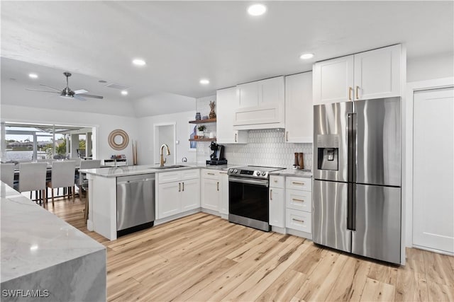 kitchen with light wood finished floors, appliances with stainless steel finishes, a peninsula, white cabinetry, and a sink