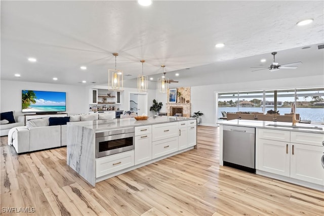 kitchen with light wood-style flooring, a sink, white cabinets, open floor plan, and appliances with stainless steel finishes