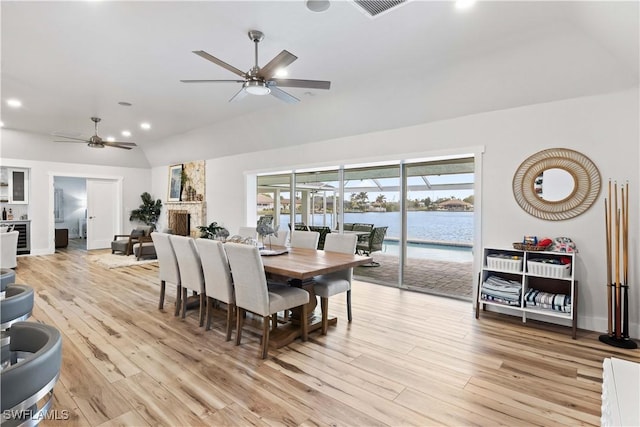 dining space with a water view, visible vents, a ceiling fan, vaulted ceiling, and light wood-type flooring