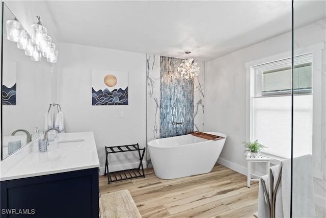 bathroom with double vanity, a sink, wood finished floors, a freestanding tub, and baseboards