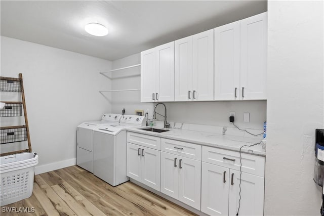 laundry room with washing machine and clothes dryer, cabinet space, light wood-style flooring, a sink, and baseboards