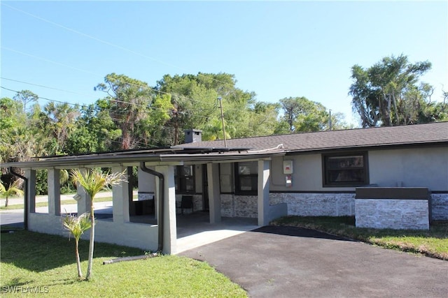 view of front of home featuring an attached carport, a front yard, driveway, stucco siding, and stone siding