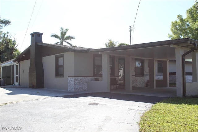 view of front of house featuring a carport, a chimney, driveway, and stucco siding