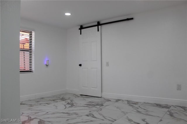 empty room featuring recessed lighting, a barn door, baseboards, and marble finish floor