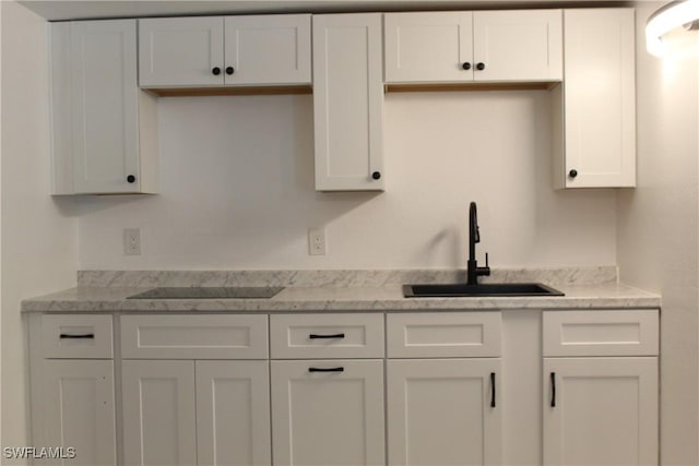 kitchen featuring white cabinets, light stone countertops, black electric stovetop, and a sink