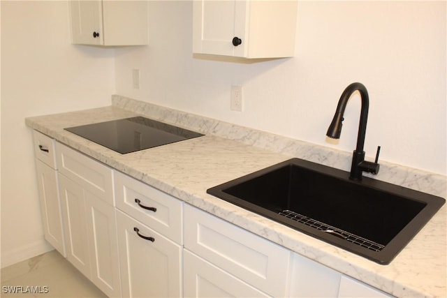 kitchen featuring marble finish floor, a sink, light stone counters, white cabinetry, and black electric stovetop