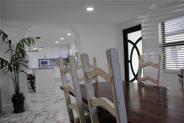 dining area featuring arched walkways, recessed lighting, and marble finish floor