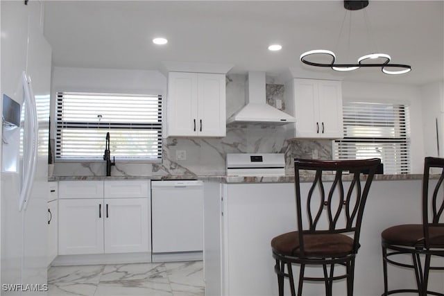 kitchen featuring white appliances, recessed lighting, decorative backsplash, white cabinetry, and wall chimney range hood