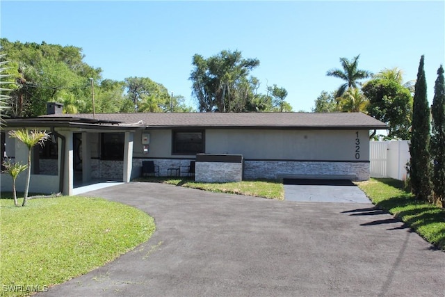 ranch-style house with a front lawn, fence, stucco siding, stone siding, and driveway