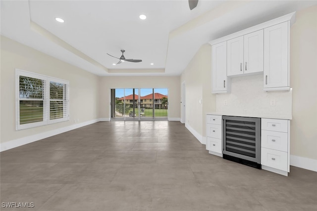 unfurnished living room with wine cooler, a tray ceiling, recessed lighting, a ceiling fan, and baseboards