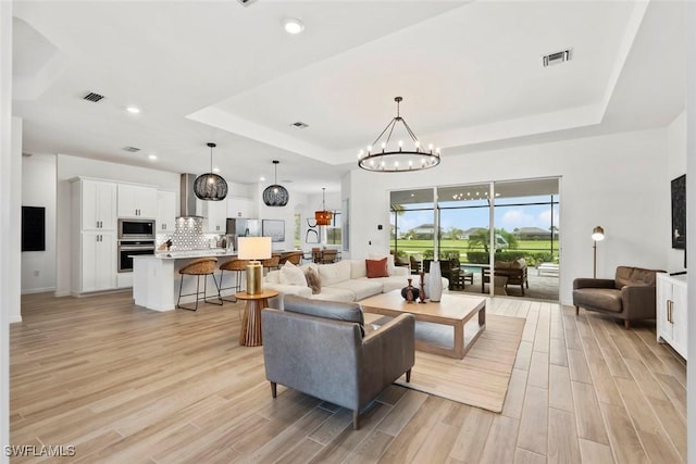 living room featuring a tray ceiling, recessed lighting, visible vents, an inviting chandelier, and light wood-style floors