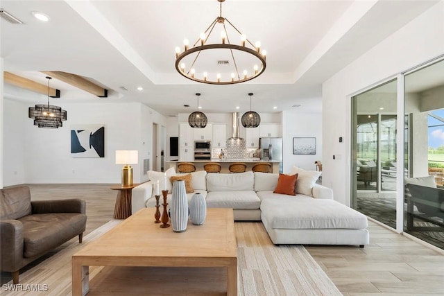 living room with light wood finished floors, visible vents, a tray ceiling, and a notable chandelier