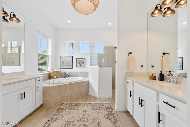 bathroom featuring walk in shower, two vanities, a sink, and a bath