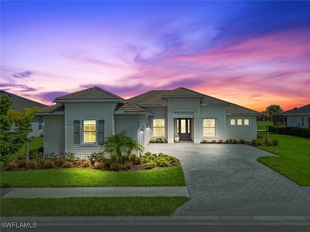 view of front of home with a tiled roof, decorative driveway, and a lawn