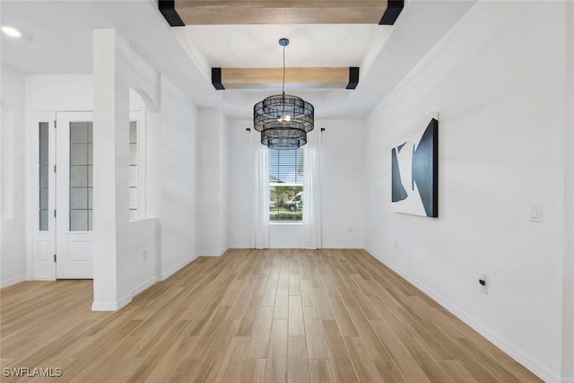 unfurnished dining area featuring a raised ceiling, a notable chandelier, light wood-style flooring, and baseboards