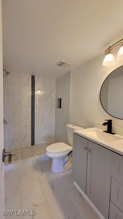 bathroom with toilet, vanity, visible vents, marble finish floor, and tiled shower