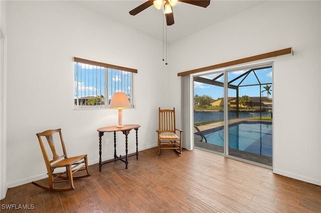 living area featuring a ceiling fan, a sunroom, baseboards, and wood finished floors