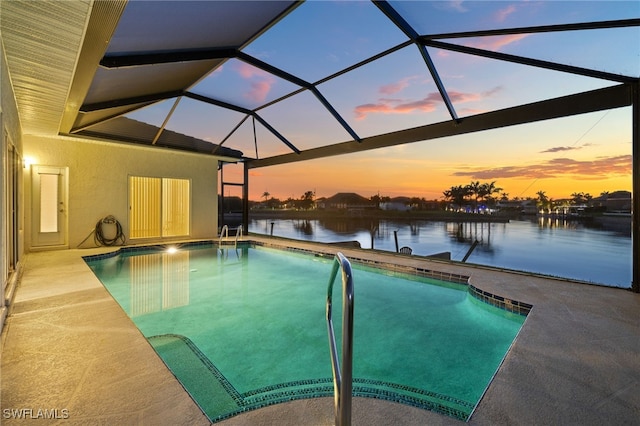 outdoor pool with glass enclosure, a patio, and a water view