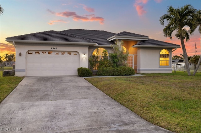 view of front of house with driveway, a lawn, a tiled roof, an attached garage, and stucco siding