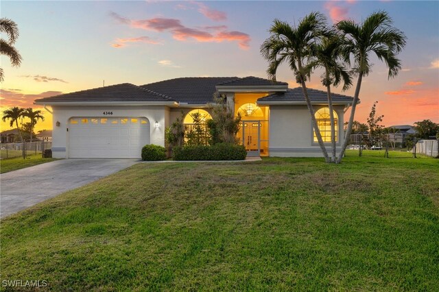 view of front facade with a yard, stucco siding, an attached garage, fence, and driveway