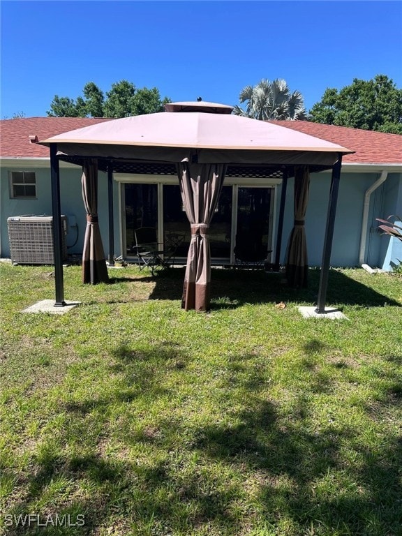 rear view of property featuring stucco siding, a lawn, central AC unit, and roof with shingles