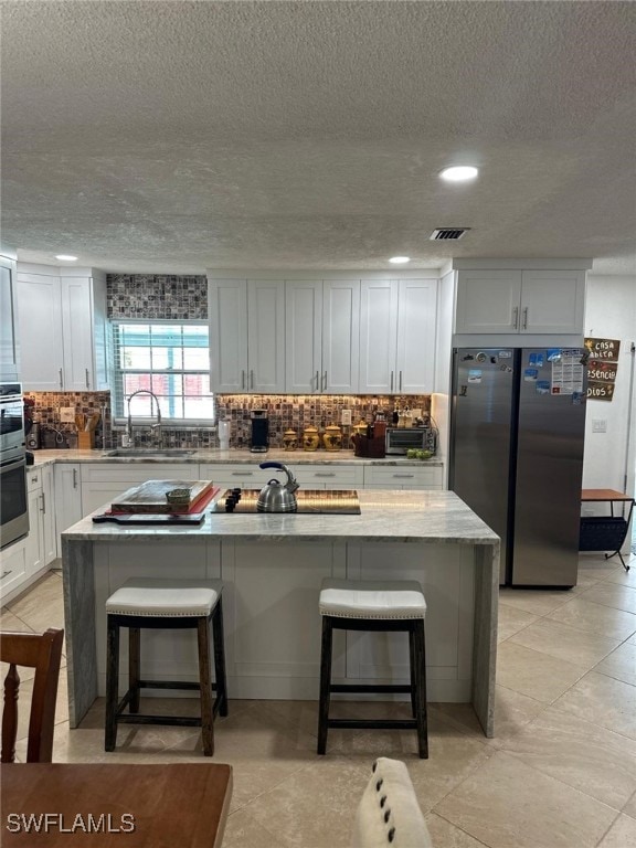 kitchen with a kitchen bar, visible vents, freestanding refrigerator, and a sink