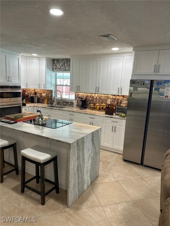 kitchen featuring a breakfast bar area, visible vents, a sink, appliances with stainless steel finishes, and tasteful backsplash