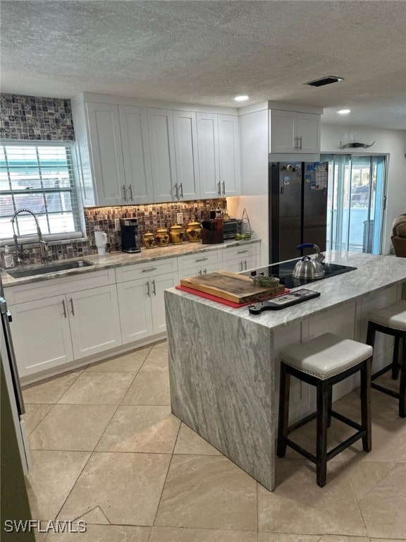 kitchen featuring tasteful backsplash, visible vents, a breakfast bar, black appliances, and a sink