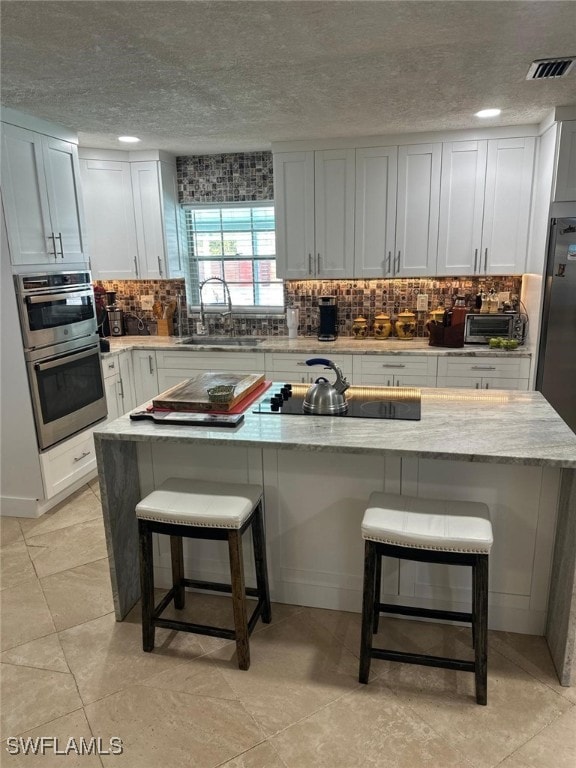 kitchen featuring black electric stovetop, a breakfast bar area, decorative backsplash, a textured ceiling, and a sink