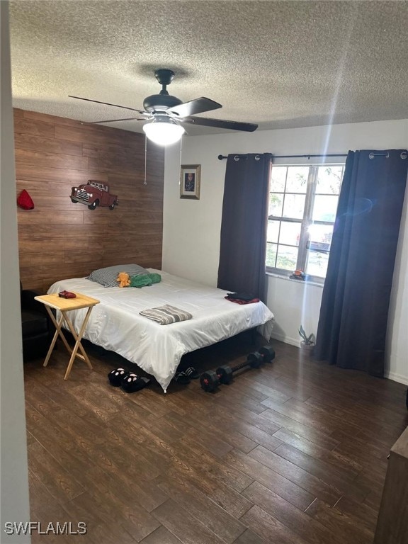 bedroom with a ceiling fan, wooden walls, wood finished floors, and a textured ceiling