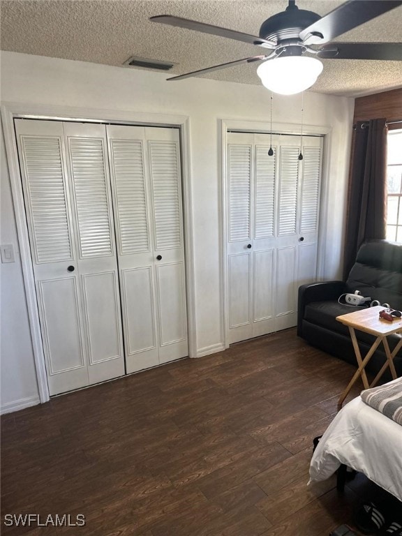 bedroom with a ceiling fan, visible vents, dark wood-type flooring, multiple closets, and a textured ceiling