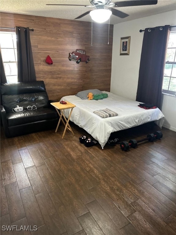 bedroom with hardwood / wood-style floors, a ceiling fan, wood walls, and a textured ceiling